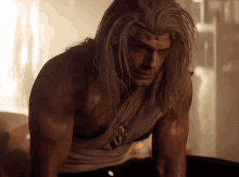 a shirtless man with long hair and a pendant on his neck