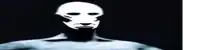 a man with a mask on his face is standing in the dark with a circle in the background .