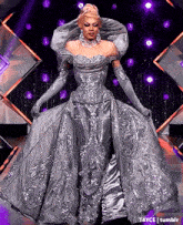 a drag queen is wearing a long silver dress and gloves .