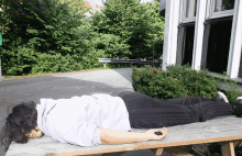 a person is laying on a picnic table in front of a green sign