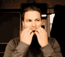 a man in a gray sweater holds his hands to his mouth