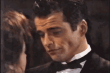 a man in a tuxedo is talking to a woman in a room .