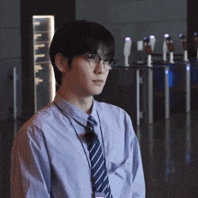 a man wearing glasses and a striped shirt stands in a hallway