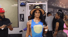 a woman wearing a hat and holding a glass of water is standing in a crowd .