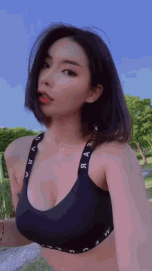 a woman in a black sports bra is standing in a park and looking at the camera .