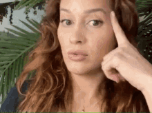 a woman with red hair is making a funny face while pointing her finger at her forehead .