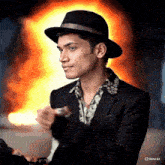 a man wearing a black hat is standing in front of a fire and the word meta is on the bottom