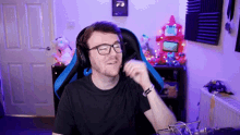 a man wearing glasses and headphones is sitting in a gaming chair and talking into a microphone .