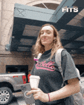a woman wearing a t-shirt that says " fits " holds a cup of coffee