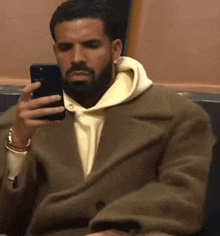 a man in a tan coat is holding a cell phone