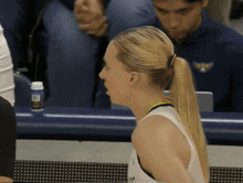 a woman in a ponytail sits at a table with a blue bottle that says ' aa ' on it