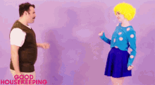 a man and a woman are dancing in front of a purple wall with the words `` good housekeeping '' written on the bottom .