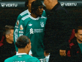 a man in a green shirt that says standard chartered is talking to another man