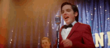 a young man in a red tuxedo is singing into a microphone .