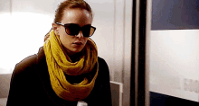 a woman wearing sunglasses and a scarf is standing in a room .
