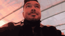 a man with a beard and a black jacket looks up at the camera