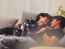 a couple of men are laying on a couch and one of them is wearing a black shirt