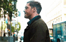 a man in a green jacket is walking down a street .