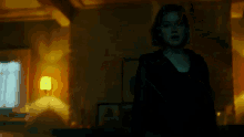 a woman in a black dress is standing in a dark room with a yellow lamp .