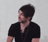 a man wearing a black shirt and a necklace looks to the side