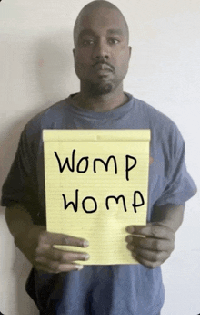 a man in a blue shirt is holding a yellow notepad with the words womp womp written on it