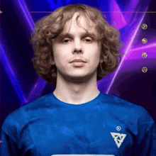 a man with curly hair is wearing a blue shirt and standing in front of a purple background .