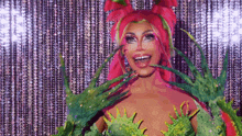 a drag queen with pink hair and green gloves is wearing a costume .