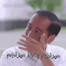 a man is covering his mouth with his hand and a foreign language is written above him .