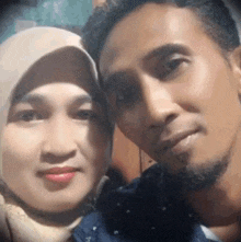 a man and a woman are posing for a picture together and the woman is wearing a hijab .