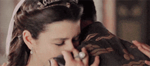 a woman with a tiara is hugging a man with a ring on her finger .