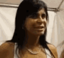 a woman with long black hair and a necklace is smiling and looking at the camera .