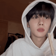 a young man wearing a white hoodie holds a straw in his hand