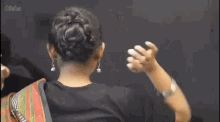 a woman wearing a black shirt and a colorful saree is tying her hair .