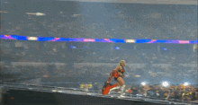 a woman in a red cape is walking on a stage in front of a crowd at a wrestling event