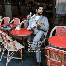 a man in a suit sits at a table reading a newspaper and says " buna dimineata good morning buenos dias "