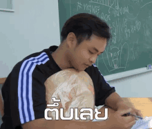 a man sits at a desk in front of a chalkboard with the word " uul " on it