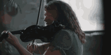 a woman with curly hair is playing a violin in front of a window .