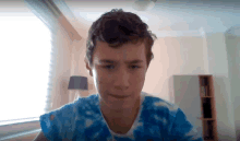 a man in a blue tie dye shirt looks at the camera