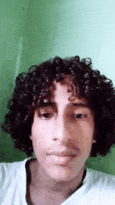 a young man with curly hair is taking a selfie with a green background .
