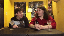 two men sitting at a table with a batman poster on the wall