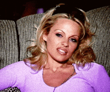 a woman is sitting on a couch wearing a purple sweater and sunglasses .