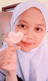 a girl in a white hijab is smiling and holding a heart shaped object in her hand