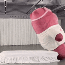 a pink stuffed animal is standing on a bed in front of a mystic story sign