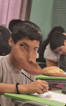 a boy with a very long nose sits at a desk in a classroom