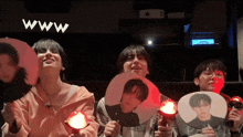 a group of people are holding fan sticks with their faces on them in front of a screen that says www .