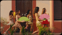 a group of women are walking down a street holding fans and one of them has a green fan