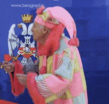 a man in a pink and yellow costume stands in front of a blue background with the website www.beograd.rs visible