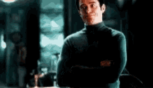 a man in a black turtleneck sweater is standing in a dark room with his arms crossed .