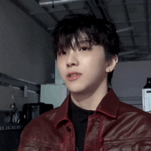 a young man wearing a red leather jacket is standing in a dark room