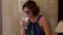 a woman wearing sunglasses drinks a martini from a glass